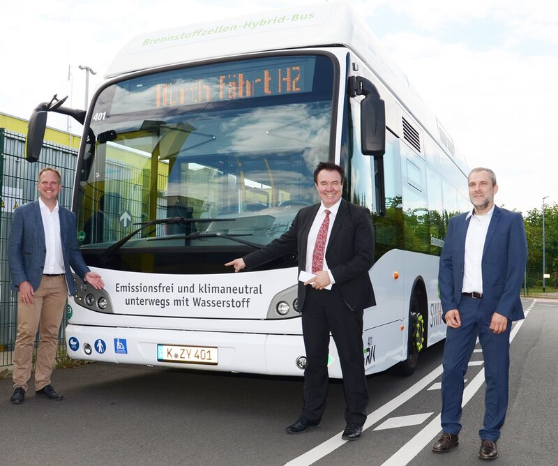 Bürgermeister Dirk Breuer, SWH-Vorstand Stefan Welsch und Carsten Bußjaeger, Prokurist und Verkehrsleiter der Regionalverkehr Köln GmbH,stehen vor einem Wasserstoff betriebenem Bus.