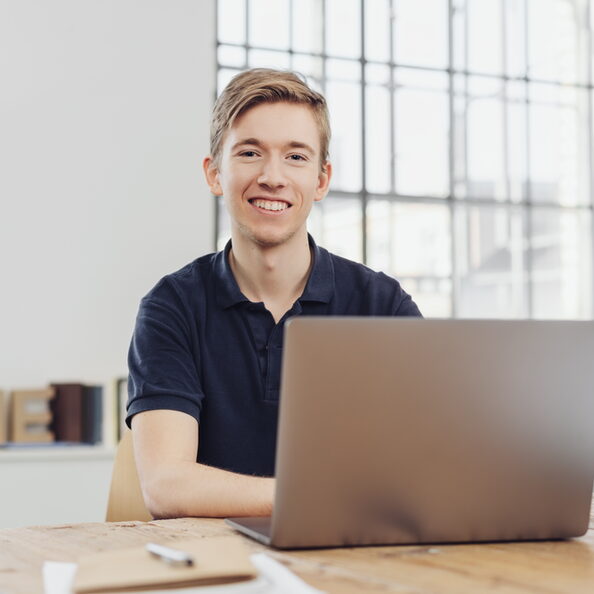 Portrait of young smiling man sitting at table in front of computer